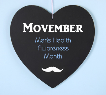 Movember fundraising for mens health awareness charity message on black heart shape blackboard on blue background.